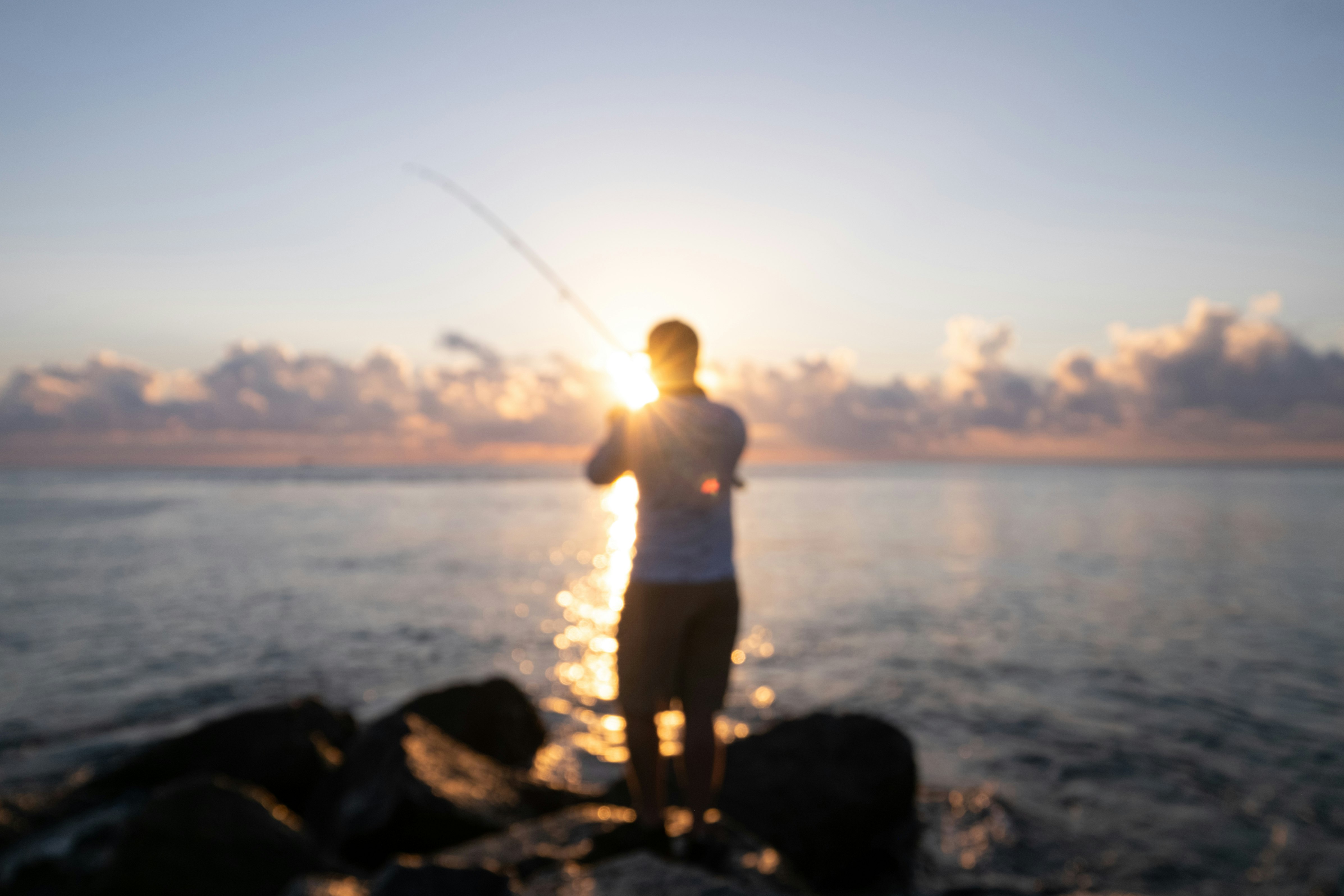 man in white shirt and black shorts fishing on sea during daytime